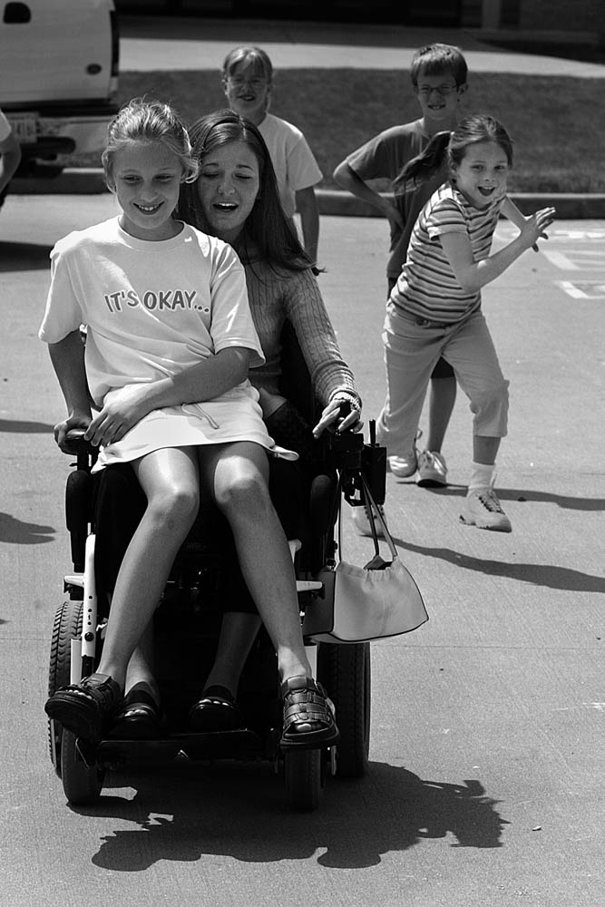 At Precious Blood School, student teacher Kelly often drew a crowd at recess who pleaded for wheelchair rides. Elizabeth Theil was the lucky rider on this day.
